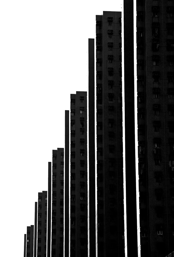 Black and white image of towering apartment buildings creating a rhythmic pattern of vertical lines against an empty sky.