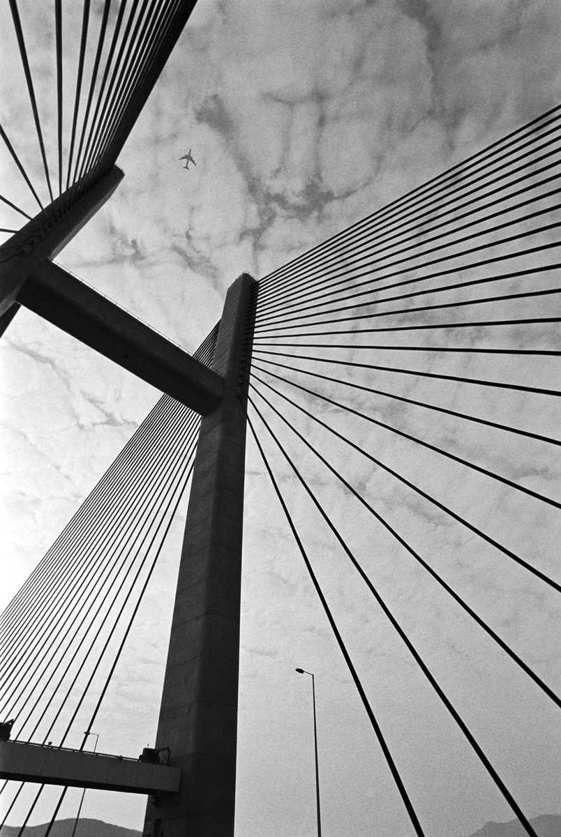 Black and white photograph of a cable-stayed bridge in Hong Kong with dramatic architectural geometry by Francis Keating