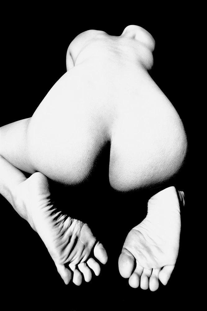 Abstract black and white nude study of a crouched female figure transformed into a sculptural form through light and shadow against a black background.