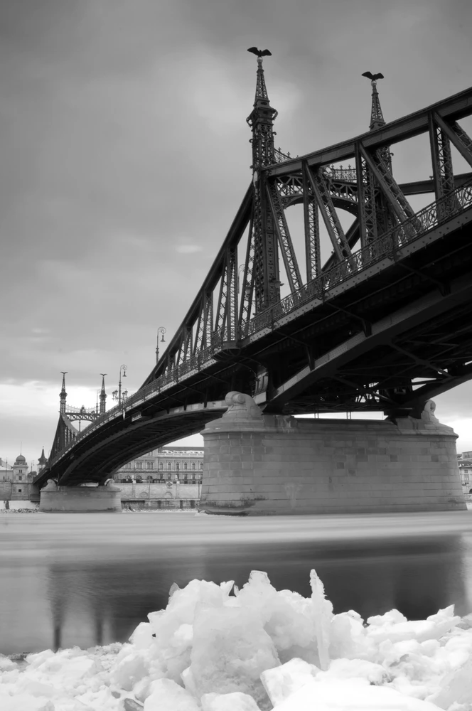 Black and white long-exposure photograph of Budapest's Liberty Bridge rising above the ice-covered Danube in winter.