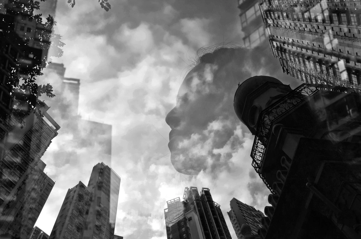 Multiple exposure portrait of a woman layered with Hong Kong skyscrapers and dramatic clouds, creating a dreamlike black and white urban composition.