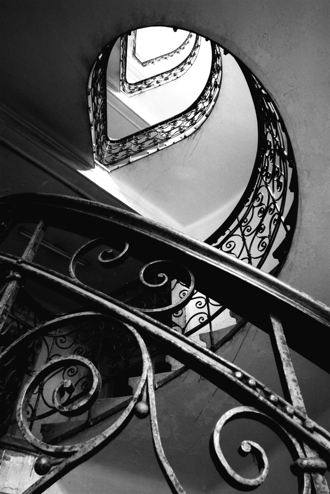 Black and white fine art photograph of a spiral staircase with wrought iron railings and geometric curves.